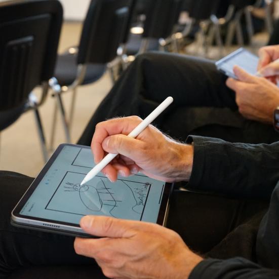 voksen person sidder og tegner med en pen på en ipad