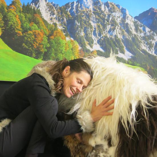 Foto af kvinde som aer en stor hund. Bjerglandskab i baggrunden.