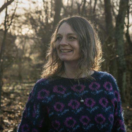 portrætfoto af Charlotte Weitze i en blå bluse med bare træer i baggrunden