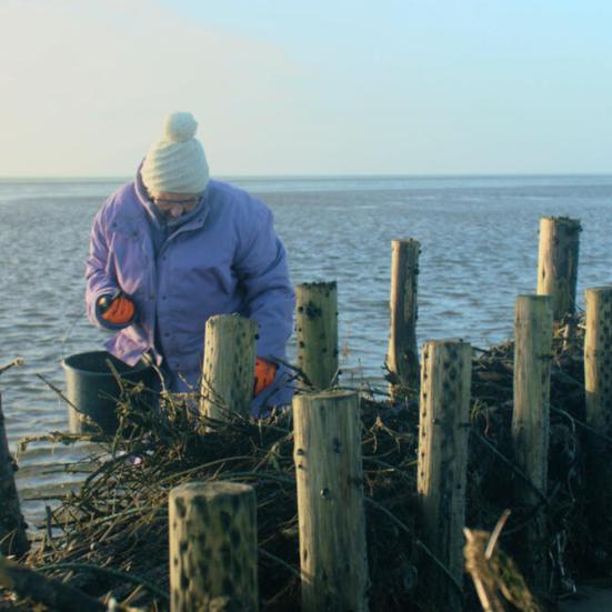 Kvinde med hue på ude ved havet pæle og vand i baggrunden
