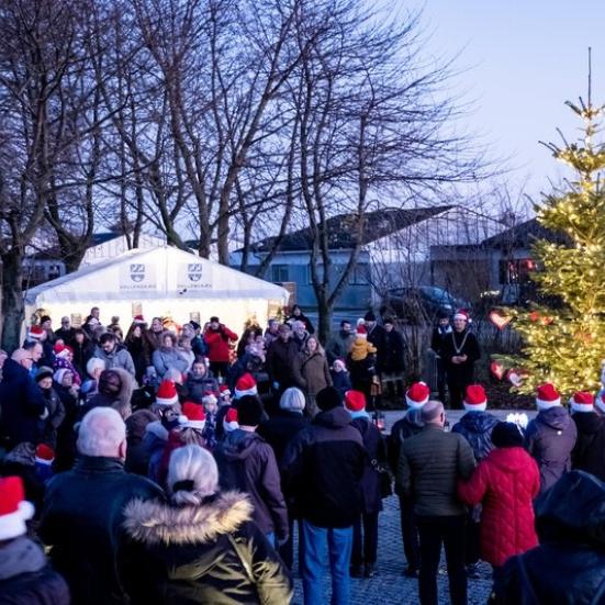 Mange mennesker der står ved Vallensbæk rådhus foran boder og et juletræ med lys i, med nissehuer på