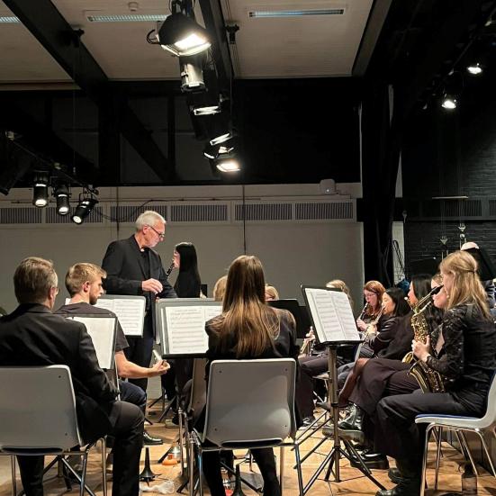 En mand med briller, der dirigere flere mennesker med instrumenter i et symfoniorkester 