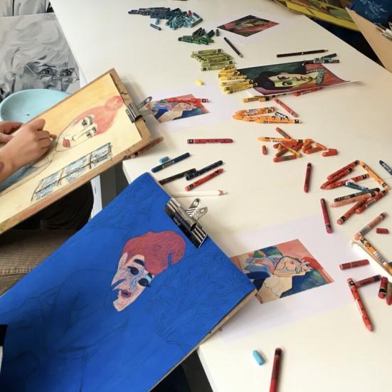 Billede af tegne sager på et bord og unge mennesker der laver kunst.