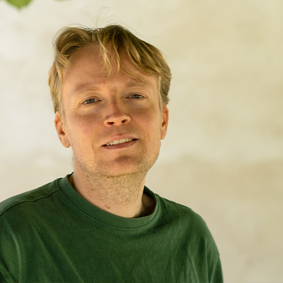 Mand der står foran en væg o grøn trøje og ser ind i kameraet