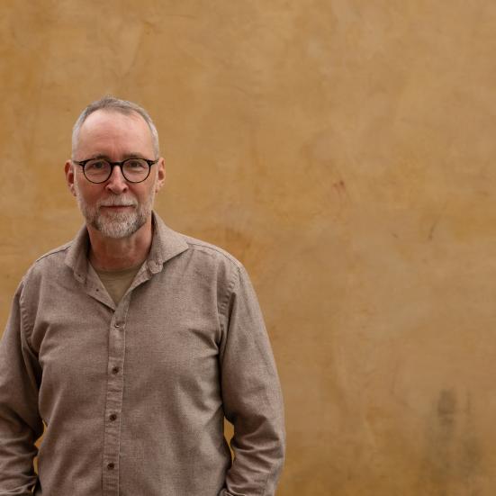 Mand med briller der står foran en væg og ser ind i kameraet