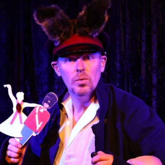 Mand med en stor hat og to dukker i hånden der ser ind i kammerat 