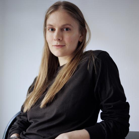 Kvinde med langt hår og en sort bluse sidder og ser ind i kammaret