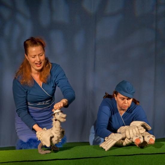 To kvinder der føre nogle dukker, foran et blåt gardin