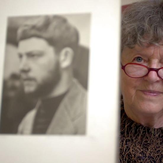 En ældre kvinde med briller der viser et sort hvidt billede frem af en mand