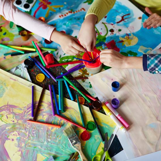 Børnehænder der rækker ind over papir, maling og pensler