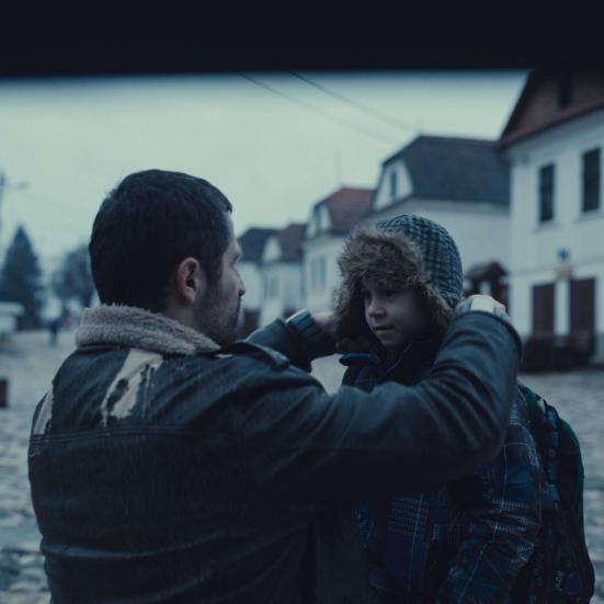 En mand på knæ der giver en dreng en varm hue på