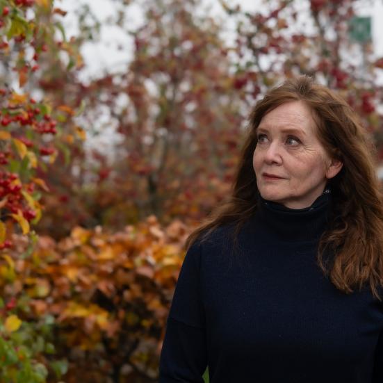 Kvinde i en sort trøje, der står udenfor i et efterårslandskab ved en busk med røde bær og ser på busken