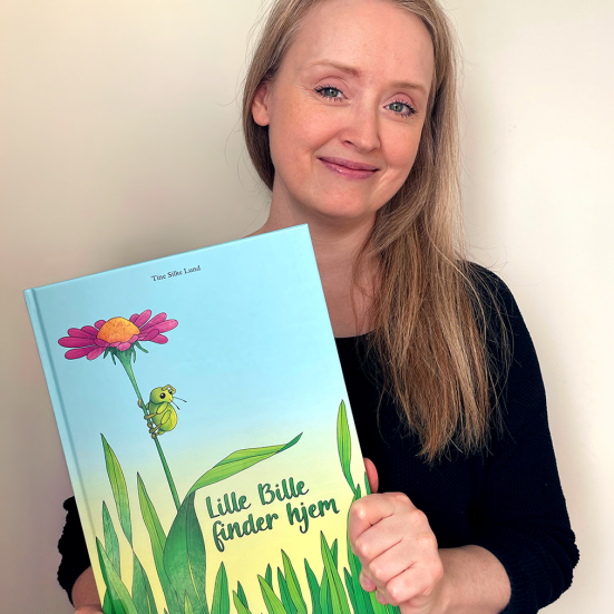 Kvinde med langt lyst hår holder en blå bog med en blomst og græs på