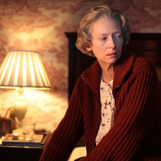 Stillbillede af Tilda Swinton fra filmen, siddende på sengekant i dæmpet belysning