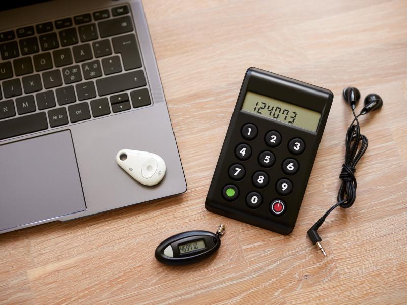 En PC og en kodeviser, kodeoplæser, samt chip på et bord med høretelefoner, hjælpemidler til at benytte sit MitID