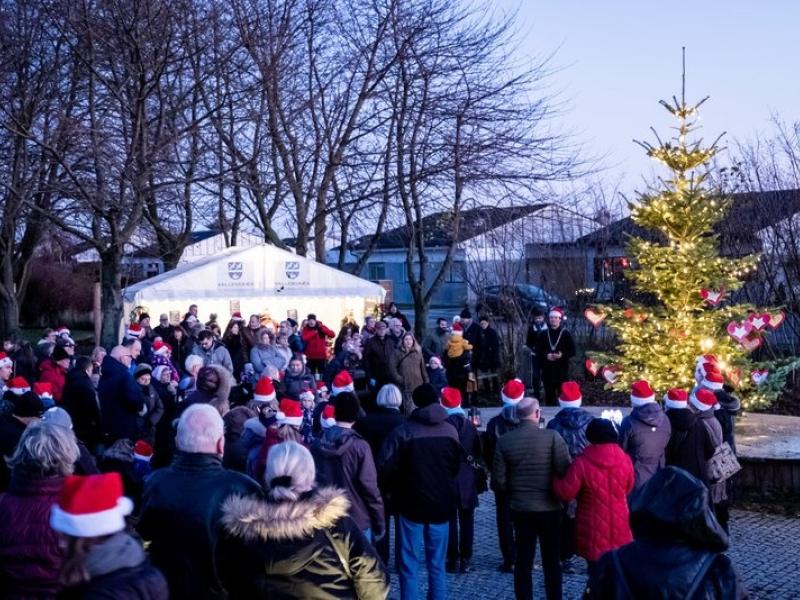 Mange mennesker der står ved Vallensbæk rådhus foran boder og et juletræ med lys i, med nissehuer på