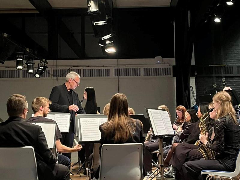 En mand med briller, der dirigere flere mennesker med instrumenter i et symfoniorkester