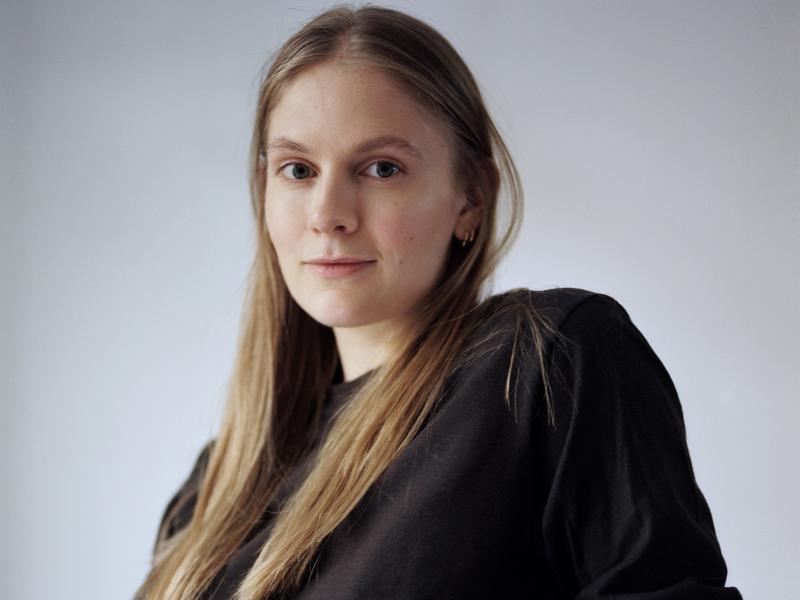 Kvinde med langt hår og en sort bluse sidder og ser ind i kammaret