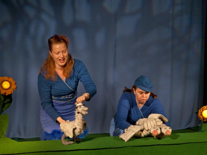 To kvinder der føre nogle dukker, foran et blåt gardin