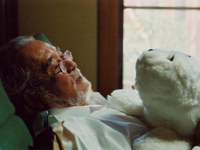 Ældre mand der ligger ned i en seng med en mekanisk bamse på brystet