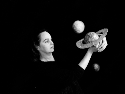 billede i sort-hvid af en kvinde der kigger eftertænksom på nogle planeter hun holder