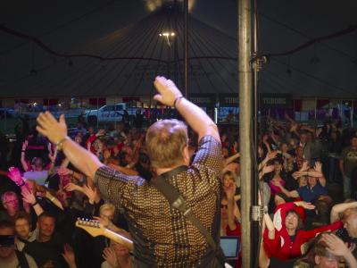 Mand der står på en scene med guitar og vinker til publikum