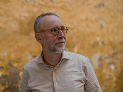 En mand med briller og skjorte på, han ser til siden og der er en gul bagrund