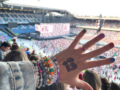 en hånd er holdt op foran en scene og publikum. tallet 13 står på håndryggen og der er en hel masse armbånd om håndleddet