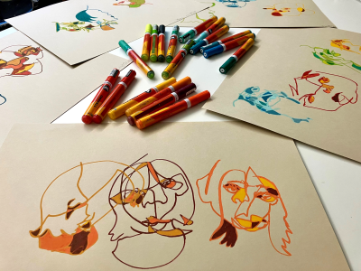 farver og tegninger af lidt abstrakte ansigter spredt ud over et bord