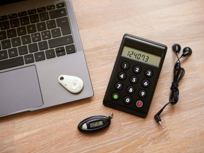 En PC og en kodeviser, kodeoplæser, samt chip på et bord med høretelefoner, hjælpemidler til at benytte sit MitID