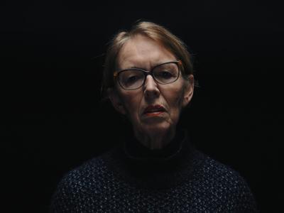 En kvinde foran en sort baggrund, hun har briller og hendes ansigt er belyst oppefra