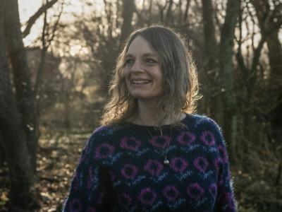 portrætfoto af Charlotte Weitze i en blå bluse med bare træer i baggrunden