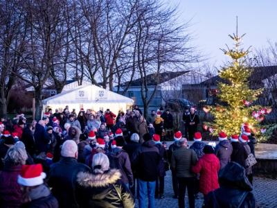 Mange mennesker der står ved Vallensbæk rådhus foran boder og et juletræ med lys i, med nissehuer på