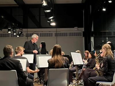 En mand med briller, der dirigere flere mennesker med instrumenter i et symfoniorkester 