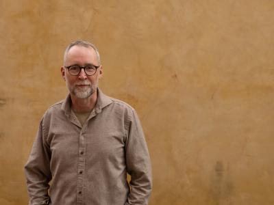 Mand med briller der står foran en væg og ser ind i kameraet