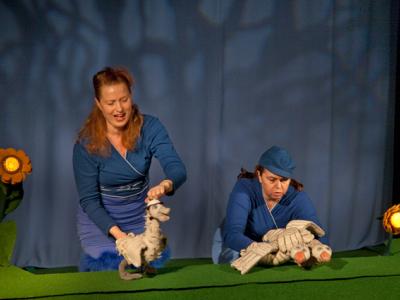 To kvinder der føre nogle dukker, foran et blåt gardin