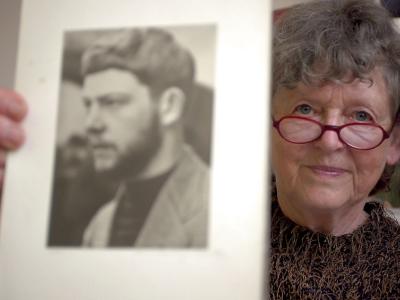 En ældre kvinde med briller der viser et sort hvidt billede frem af en mand