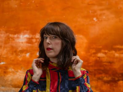 Kvinde foran en orange murstensmur i en farvestålende jakke