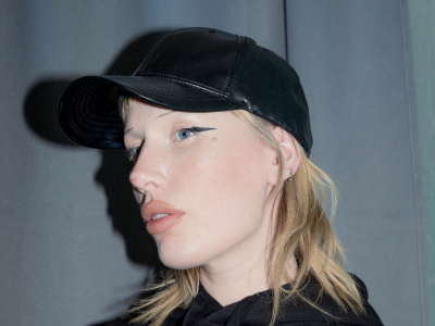 Foto af ung blond kvinde med sort hættetrøje og kasket og cubernauternes logo i pink i bunden