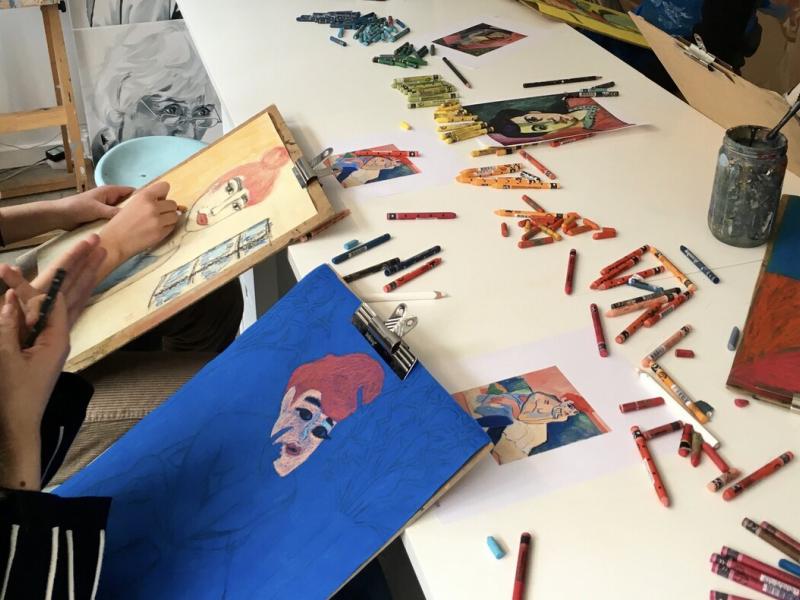 Billede af tegne sager på et bord og unge mennesker der laver kunst.