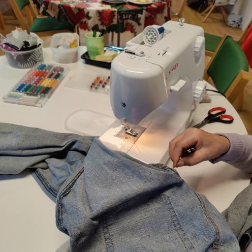 på et hvidt bord er en symaskine og en masse sygrej, en person er i gang med at arbejde på et par blå jeans