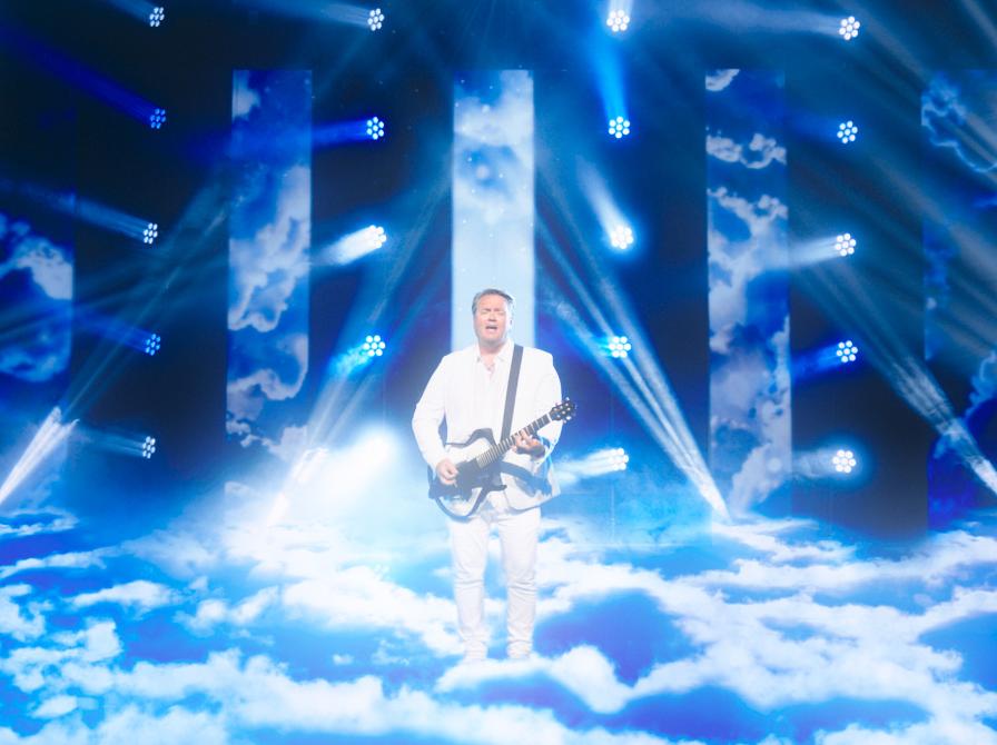 Mand der står på en scene med guitar og sport lys