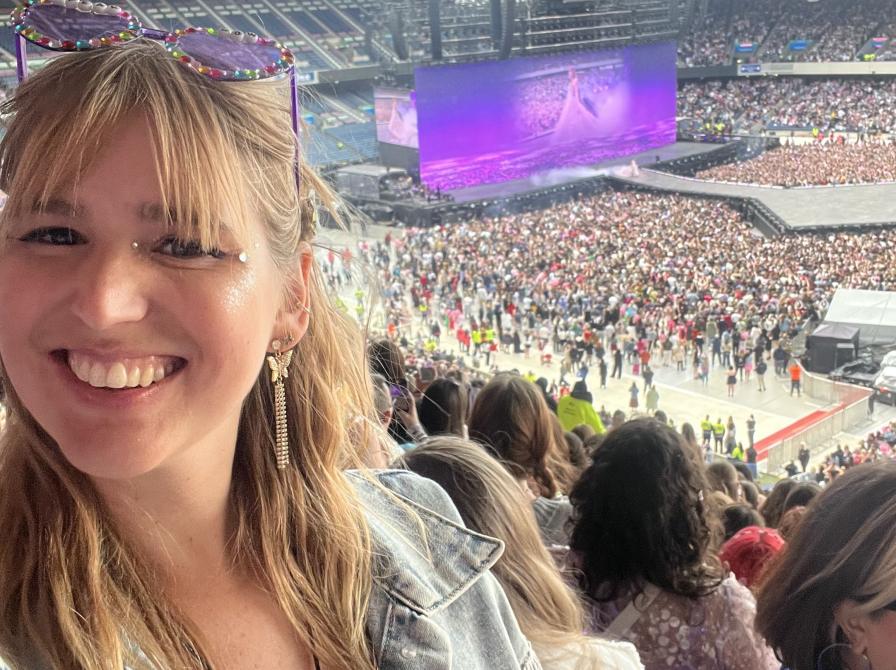 Billede af kvinde der smiler til en koncert med mange mennesker i baggrunden og storskærm med Taylor Swift på