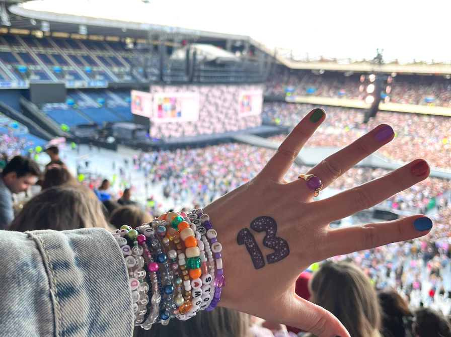 en hånd er holdt op foran en scene og publikum. tallet 13 står på håndryggen og der er en hel masse armbånd om håndleddet