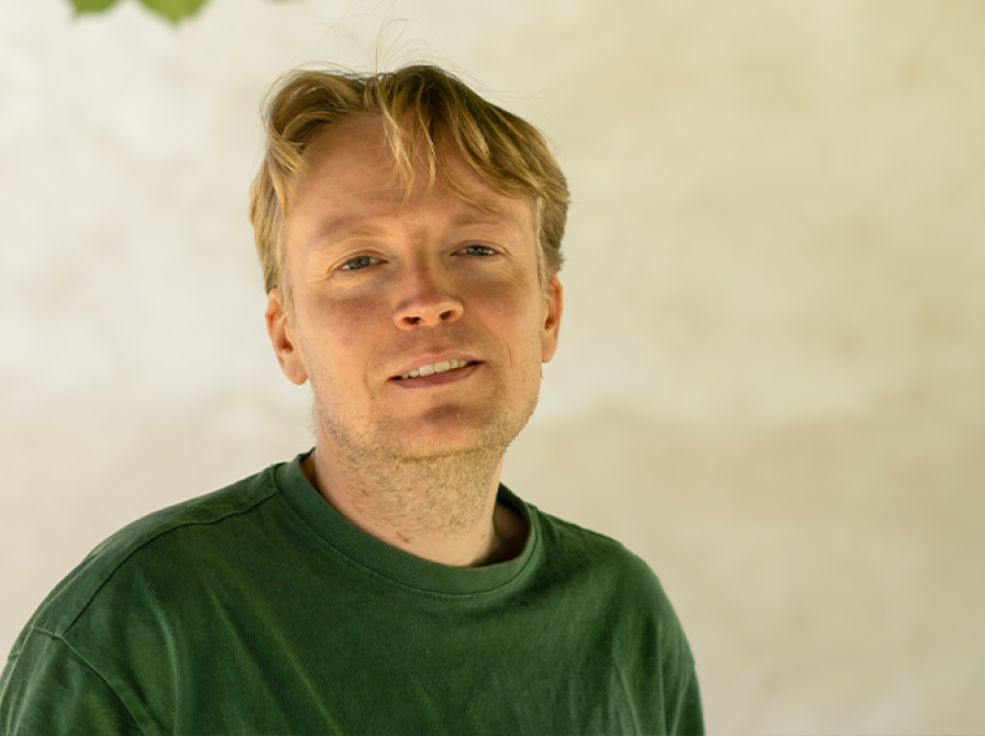 Mand der står foran en væg o grøn trøje og ser ind i kameraet