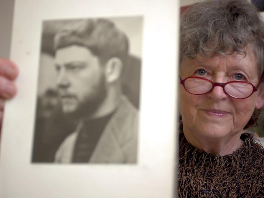 En ældre kvinde med briller der viser et sort hvidt billede frem af en mand