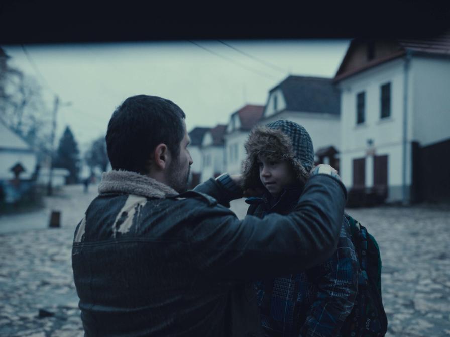 En mand på knæ der giver en dreng en varm hue på