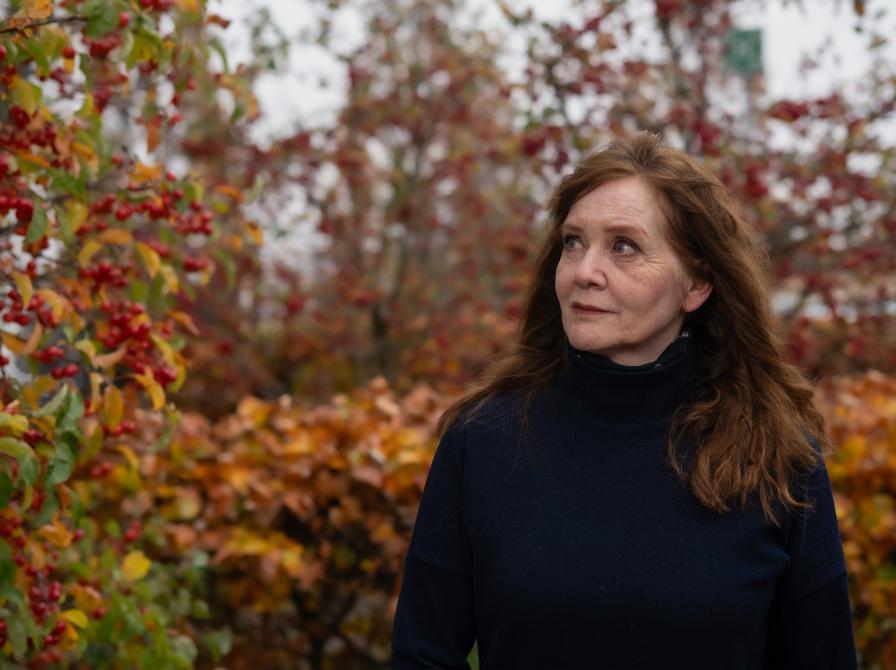 Kvinde i en sort trøje, der står udenfor i et efterårslandskab ved en busk med røde bær og ser på busken